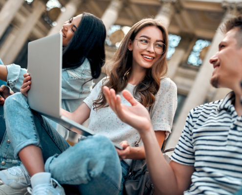 A group of students with laptops sit on the steps near the campu