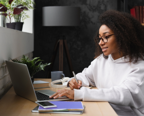 Teenager e-learning on distance, using laptop, writing homework, watching webinars online from home.